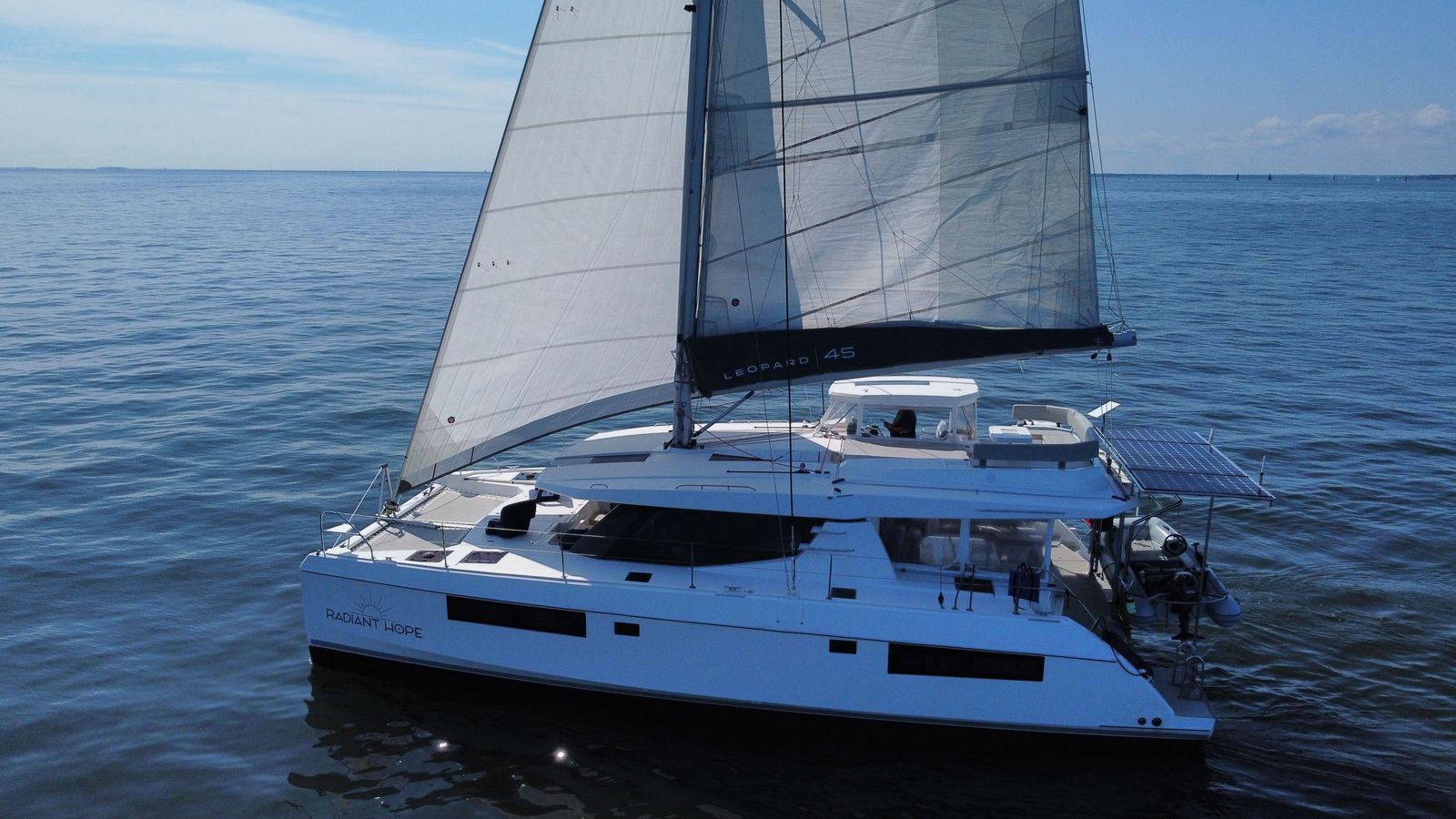 Catamaran under sail on open Chesapeake water, port beam, RADIANT HOPE on hull